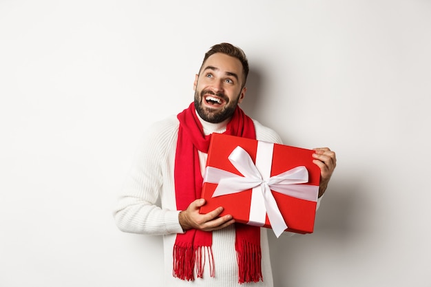 Feliz Navidad. Hombre feliz mirando extasiado y sosteniendo su regalo de año nuevo, de pie contra el fondo blanco.