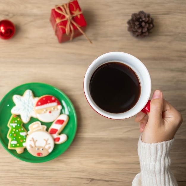 Feliz Navidad con la mano de una mujer sosteniendo una taza de café y una galleta casera en la mesa Fiesta de la víspera de Navidad y feliz concepto de Año Nuevo