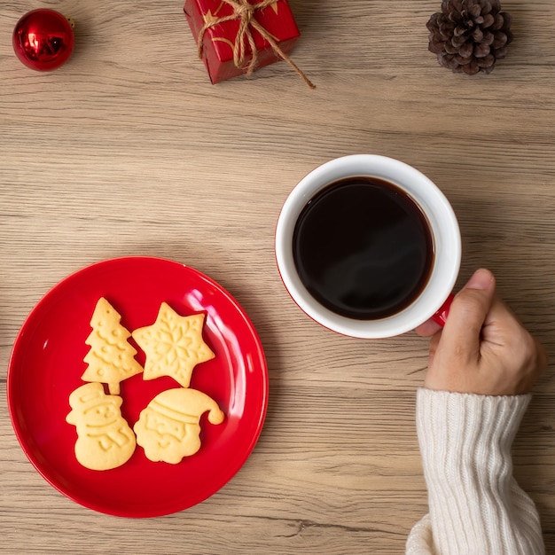 Feliz Navidad con la mano de una mujer sosteniendo una taza de café y una galleta casera en la mesa Fiesta de la víspera de Navidad y feliz concepto de Año Nuevo