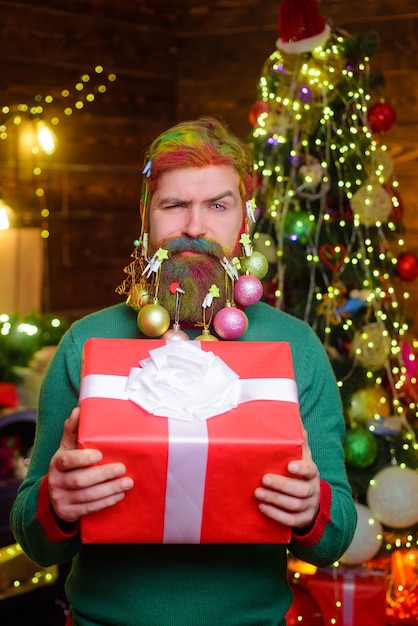 Feliz navidad y próspero año nuevo hombre barbudo con barba decorada tiene caja de regalo de navidad divertida
