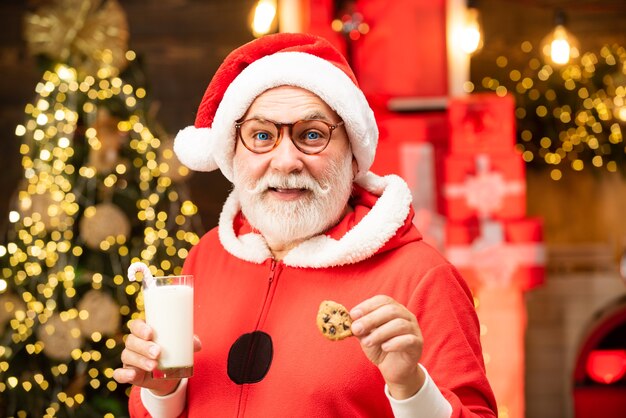 Feliz navidad santa claus comiendo una galleta y bebiendo un vaso de leche en casa ...