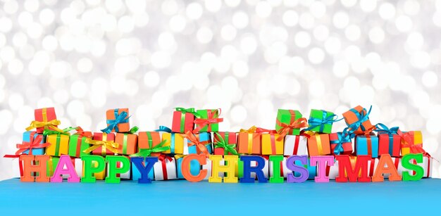 Feliz navidad texto colorido en el fondo de regalos multicolores sobre un fondo bokeh