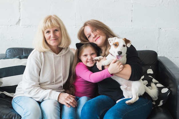 Feliz neta, avó e filha sentadas no sofá com o cachorro jack russell terrier