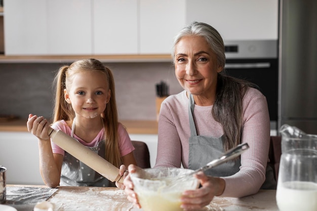 Feliz netinha europeia e chefs avós idosos manchados com farinha preparando massa