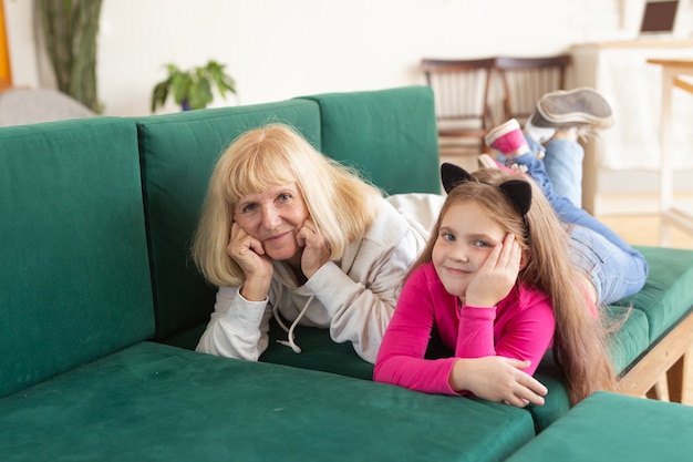 Feliz nieta y abuela acostada en el sofá en pose divertida. La abuela se divierte con su nieto en casa. Concepto de personas mayores, familia y generación.