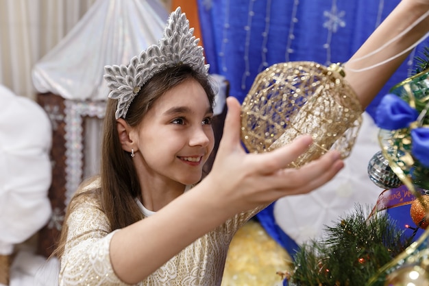 Feliz niña de 10 años decorando el árbol de navidad en casa interior.