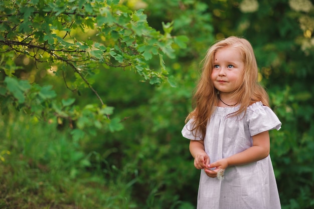 Feliz niña de 3 años en vestido blanco está jugando en el jardín de verano de la aldea