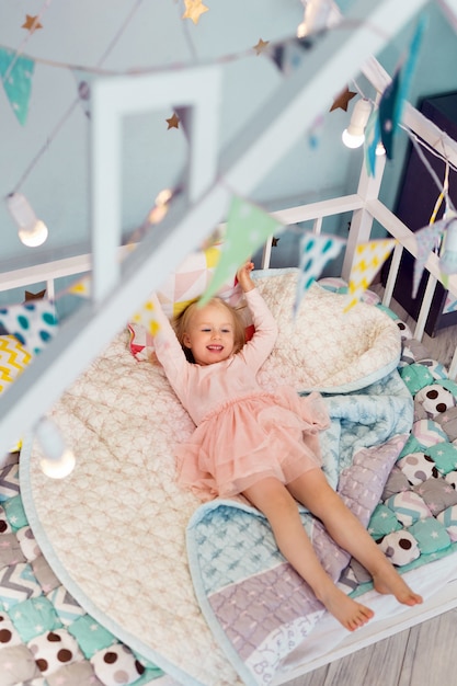 Feliz niña de 3 años con un vestido rosa acostada en una cama acogedora. Vista superior. Vista desde arriba