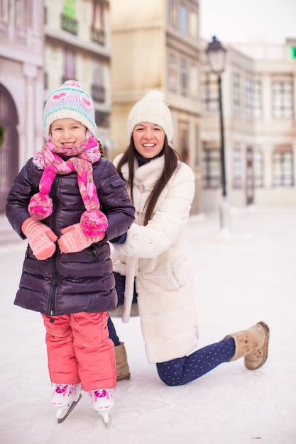 Feliz niña adorable y joven madre patinando sobre hielo