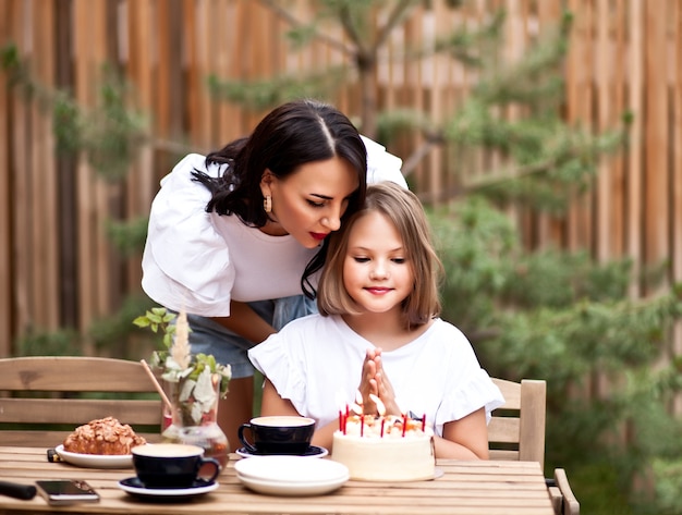 Feliz niña adorable con mamá celebrar con pastel de cumpleaños en la terraza del café. 10 años celebran cumpleaños.