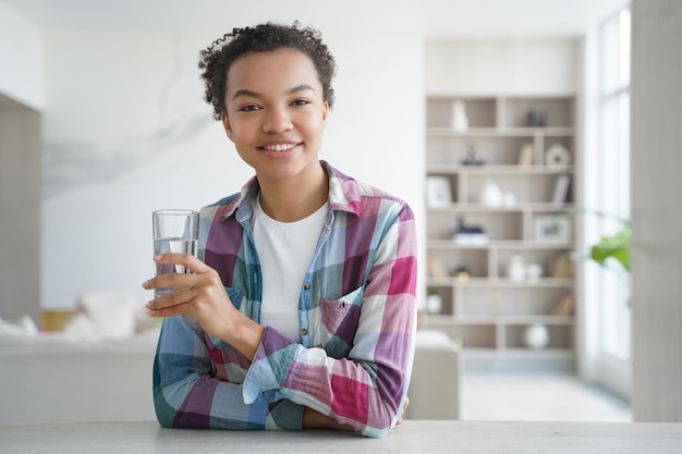 Feliz niña afroamericana bebe agua de un vaso Rutina de salud matutina de estilo de vida saludable