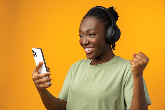 Feliz niña afroamericana sonriente usando su teléfono inteligente en estudio amarillo
