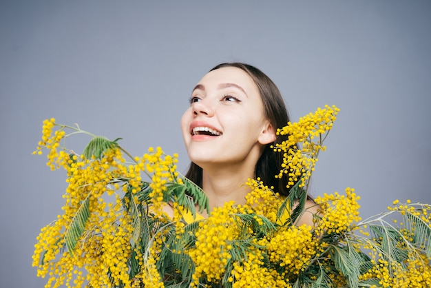 Feliz niña alegre sonriendo, sosteniendo mimosa fragante amarilla