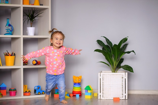 Feliz niña de un año corre jugando en el jardín de infantes, en casa