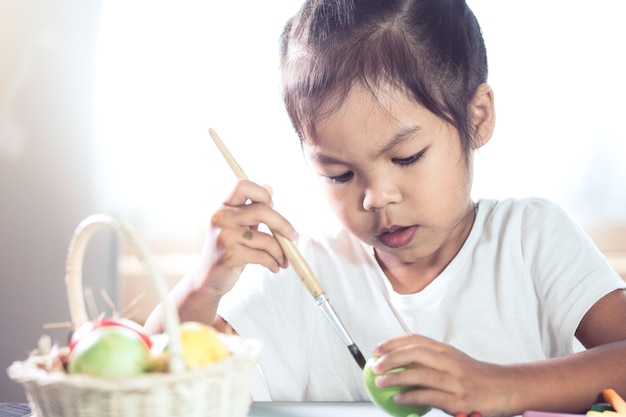 Feliz niña asiática dibujo y pintura en el huevo de Pascua