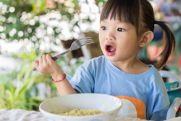 Feliz niña asiática disfruta comiendo algunos fideos por sí misma.