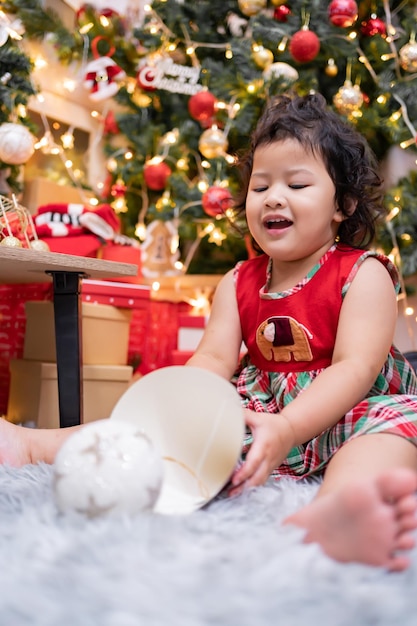 Feliz niña asiática divertirse el día de Navidad. Niño con padre con decoración de árbol de Navidad en casa de vacaciones.