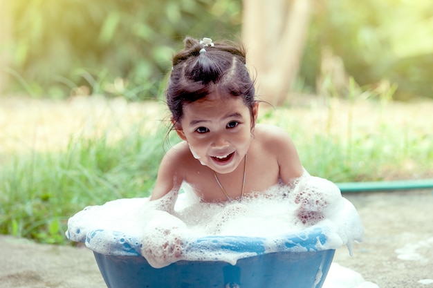 Feliz niña asiática divirtiéndose y jugando con espuma