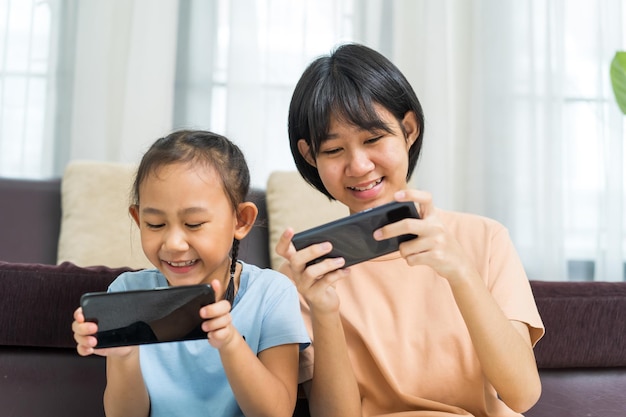 Feliz niña asiática con hermana jugar juntos en el teléfono inteligente en casa