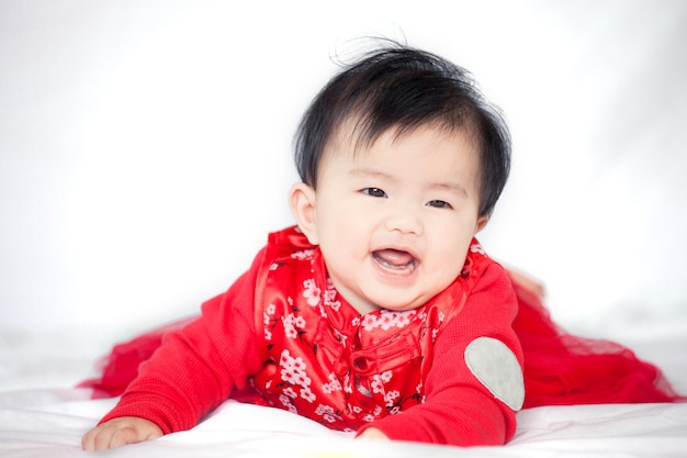 Feliz niña asiática linda en traje de tradición china sonriendo y gateando en la cama