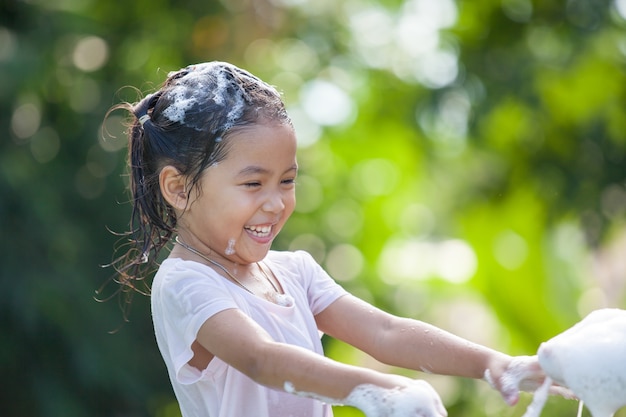 Feliz niña asiática niño divirtiéndose para bañarse y jugar con espuma en el exterior