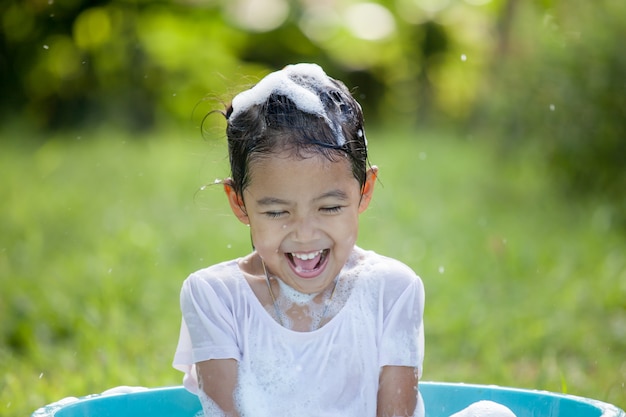 Feliz niña asiática niño divirtiéndose para bañarse y jugar con espuma en el exterior