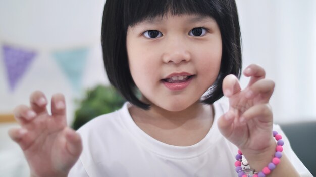 Foto feliz niña asiática que pretende ser monstruo haciendo una cara de miedo