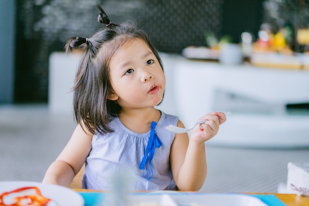 Feliz niña asiática uso tenedor y comiendo salchicha