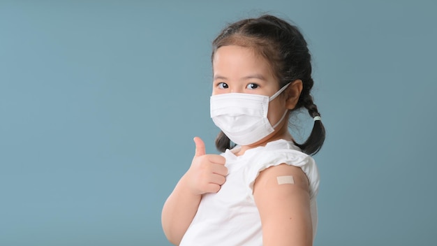 Feliz niña asiática vacunada mostrando el brazo con yeso después de la inyección de la vacuna Covid19