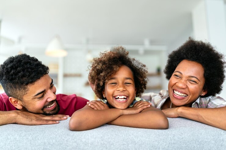 Foto feliz niña biracial sonriendo con jóvenes padres multirraciales disfrutando del fin de semana en casa juntos