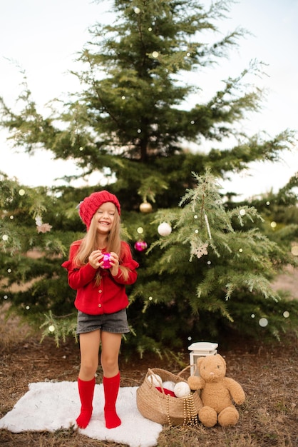 Feliz niña bonita niño usar suéter de sombrero rojo de punto y calcetines decorando el árbol de Navidad