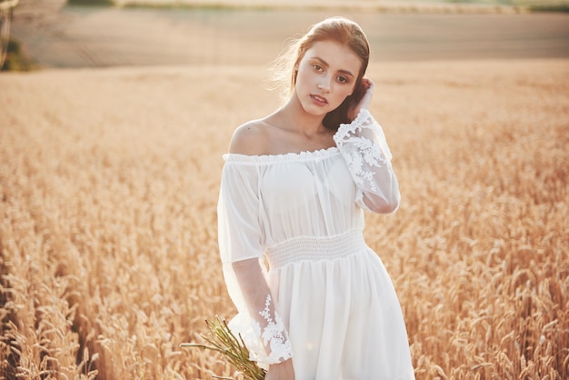 Feliz niña con cabello largo y hermoso de pie en un campo de trigo bajo la luz del sol