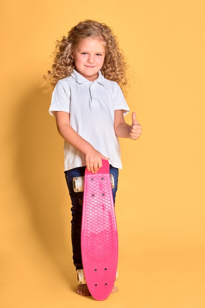 Feliz niña con cabello rizado divirtiéndose con penny board