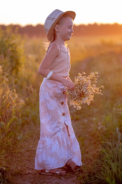 Feliz niña caucásica de 5 años con un ramo de flores de manzanilla en la pradera mirando a un lado, un retrato al atardecer