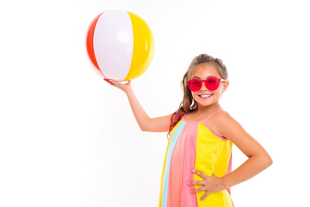 Feliz niña caucásica con ropa colorida tiene gran pelota de goma y sonríe aislado sobre fondo blanco.