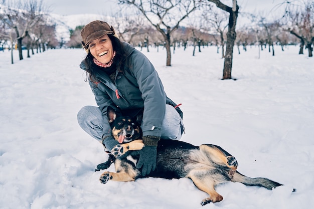 Una feliz niña caucásica sonriente agachada en la nieve abrazando a su perro con un ojo de cada color