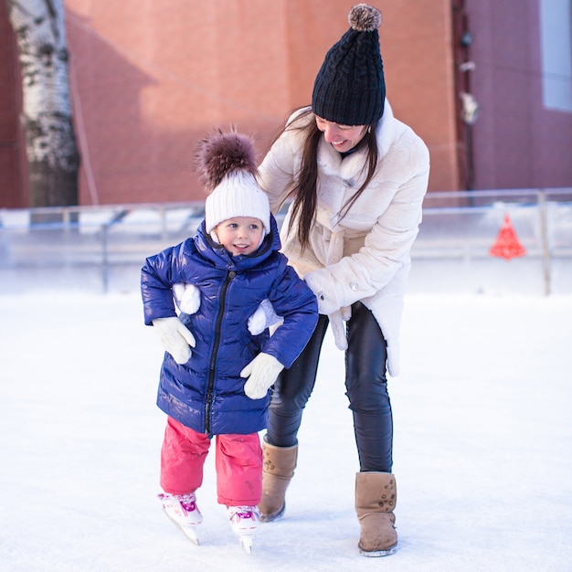 Feliz niña emocionada y su joven madre aprendiendo patinaje sobre hielo
