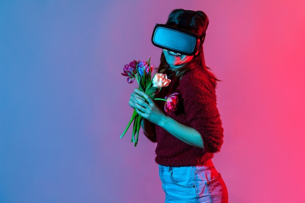 Feliz niña encantadora en auriculares de gafas Vr sosteniendo ramo de flores y sonriendo