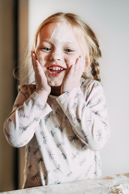 Feliz niña se encuentra en el retrato de primer plano de la cocina y tiene su propia cara