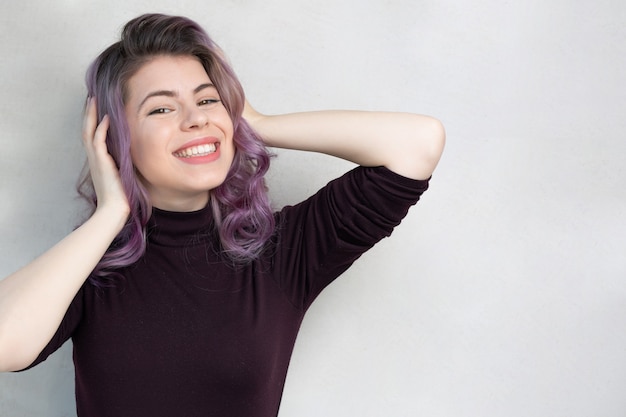 Feliz niña gloriosa con cabello morado sobre un fondo gris. Espacio para texto