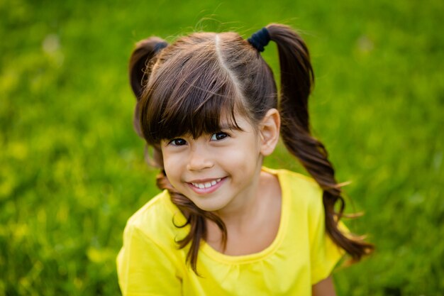 Feliz niña india en camiseta amarilla ríe verano en el césped