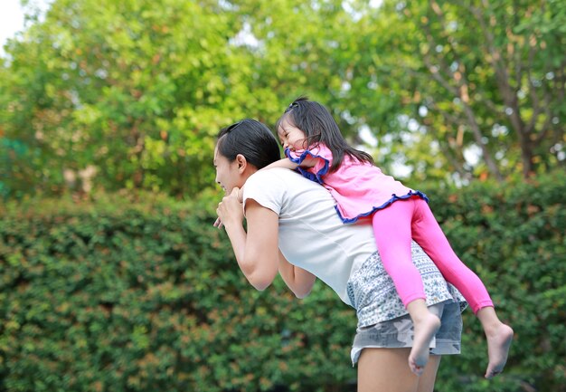 Feliz niña linda montando a la madre en el parque