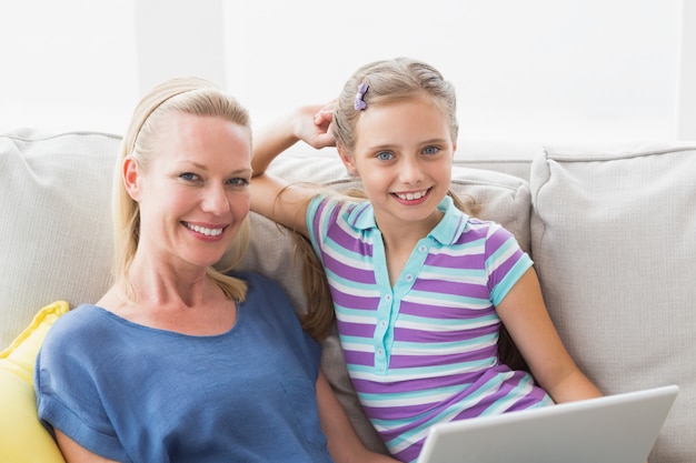 Feliz niña con madre usando la computadora portátil en el sofá en casa