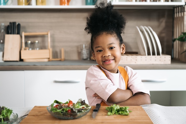 Feliz niña negra con ensalada a bordo en la cocina