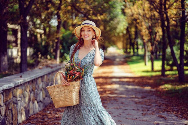 Feliz niña pelirroja sonriente en vestido revoloteando camina en el concepto de verano indio del parque de otoño