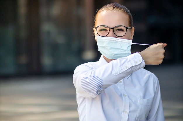 Feliz niña positiva, joven bella mujer, empresaria saca máscara médica estéril protectora de la cara al aire libre oficina de negocios, sonriendo. Final feliz. Victoria sobre el coronavirus. Pandemia Covid-19.