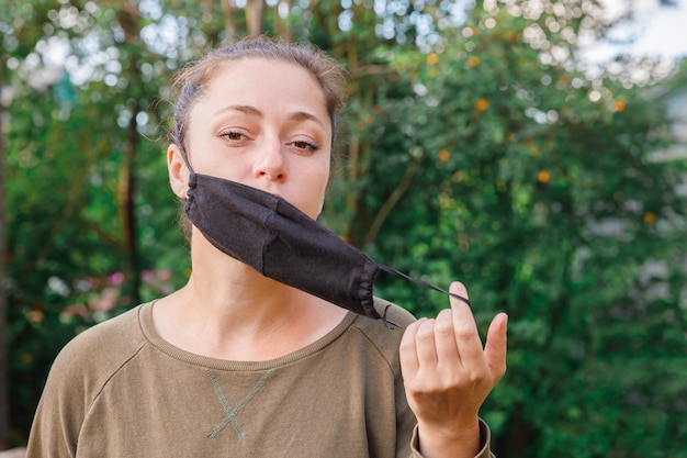 Feliz niña positiva se quita la máscara médica protectora de la cara al aire libre.