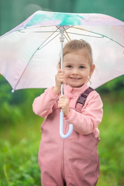 Foto feliz niña riendo de 23 años vistiendo ropa impermeable y sosteniendo un paraguas rosa diviértase en el patio trasero de su casa en un día lluvioso