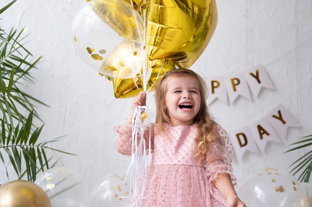 Feliz niña rubia en vestido rosa sosteniendo globos y celebrando su cumpleaños