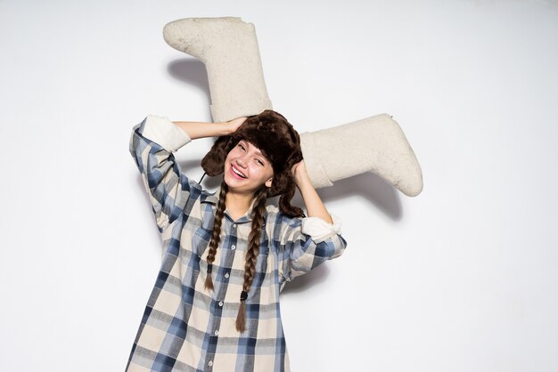 Foto feliz niña de rusia en un cálido sombrero de piel tiene botas de invierno gris
